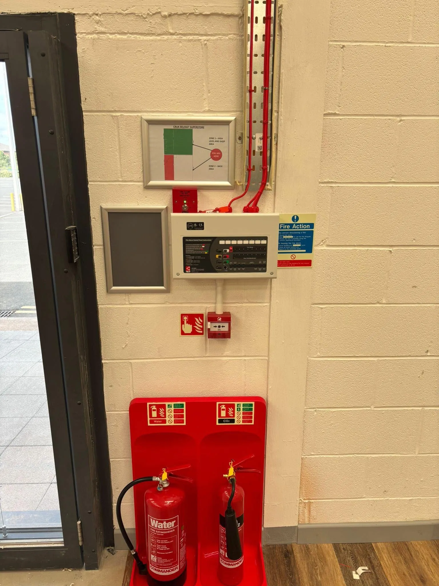 A fire alarm control panel, call point and extinguishers beside a fire exit