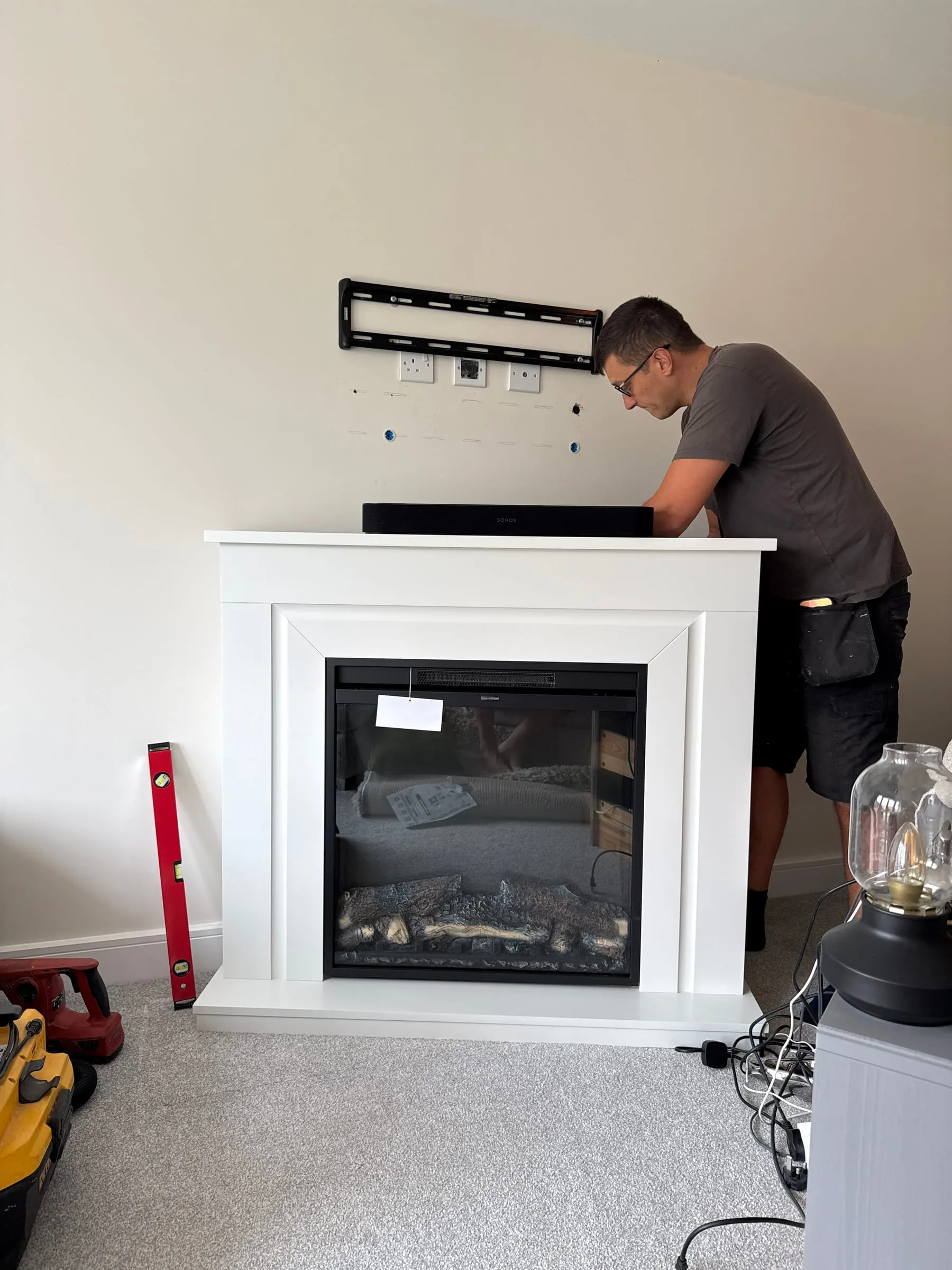 A TV bracket being fitted to the wall above a fireplace